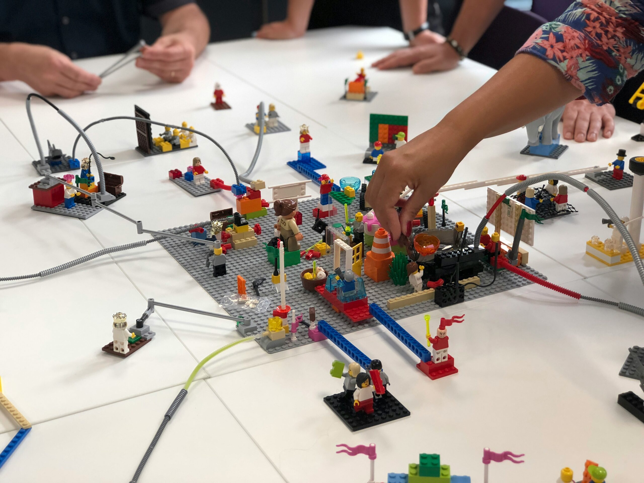 People collaborating on a LEGO build activity with interconnected structures and minifigures on a table