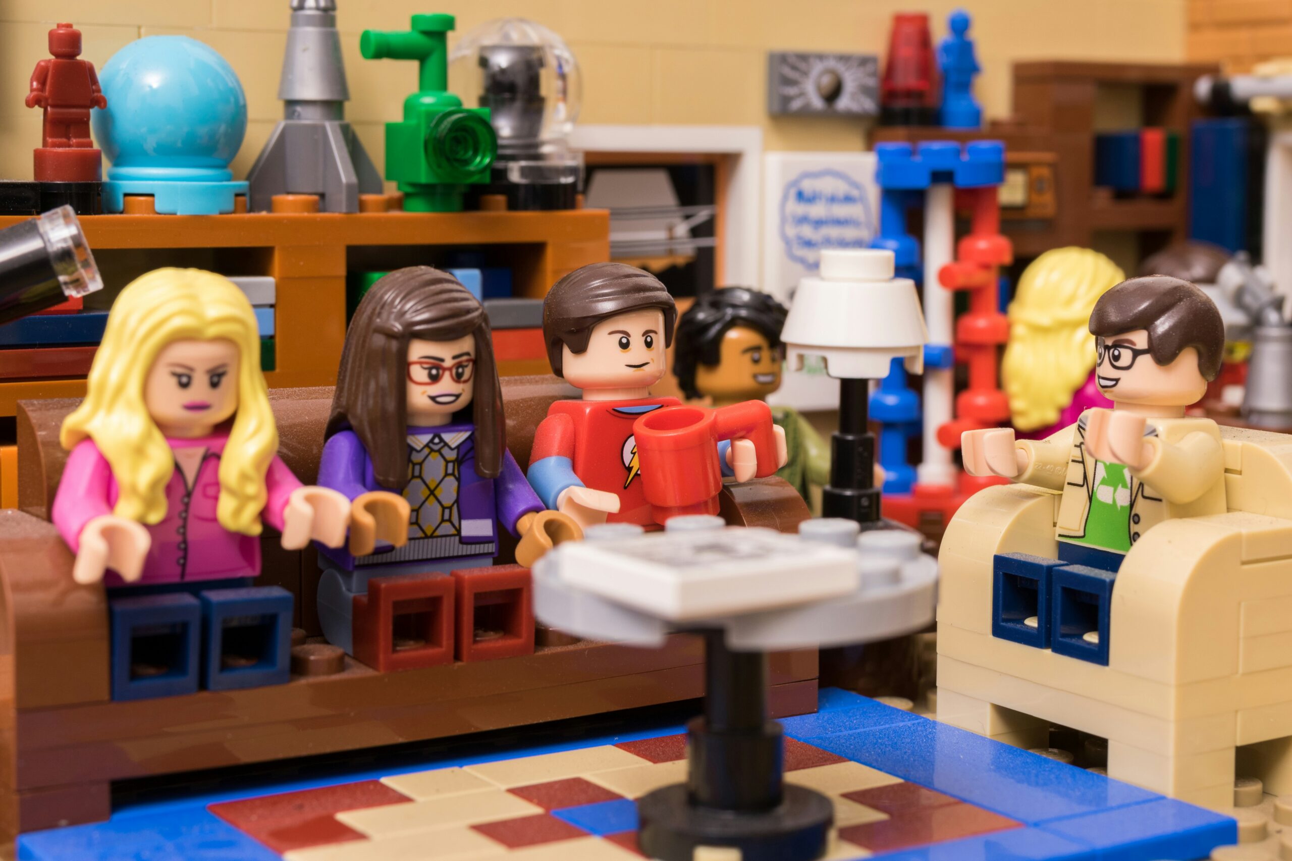 LEGO minifigures sitting in a living room scene, gathered on couches and chairs around a table in a detailed indoor LEGO set
